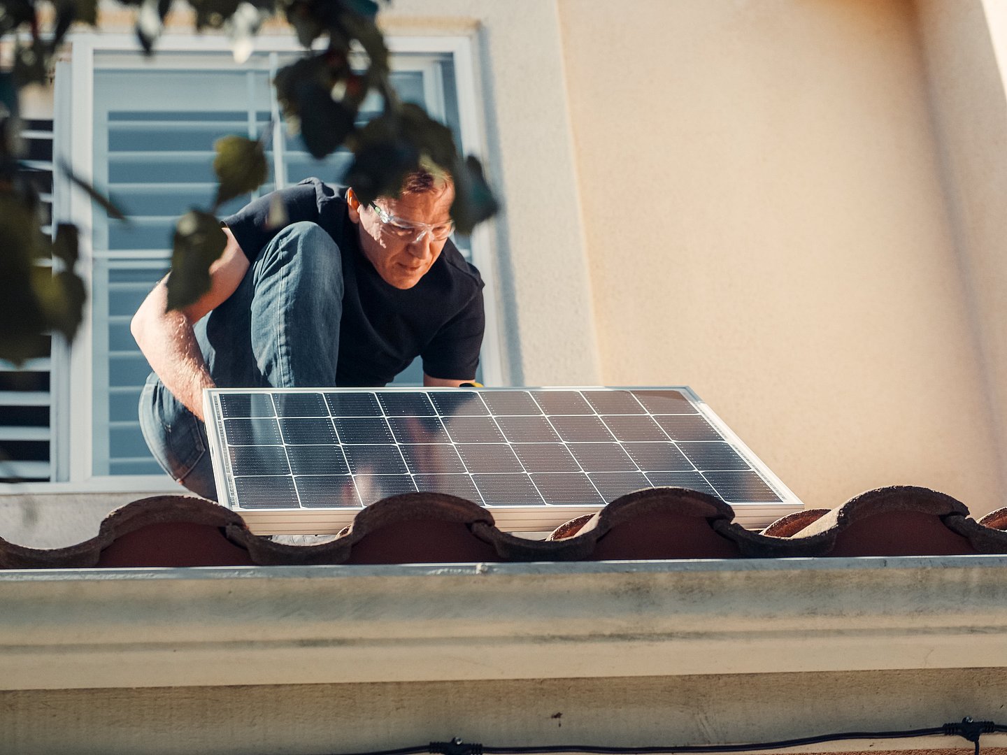 Mann mit Schutzbrille installiert kleines Solarpanel auf dem Dach